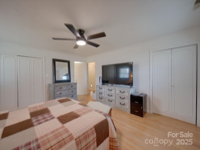 bedroom featuring ceiling fan, two closets, and light hardwood / wood-style flooring