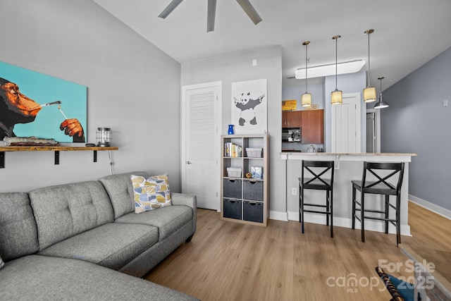 living room featuring ceiling fan, vaulted ceiling, light wood-type flooring, and baseboards