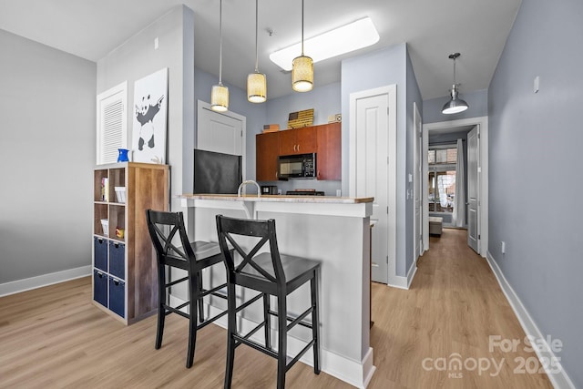 kitchen featuring black microwave, a breakfast bar, light wood-style flooring, and baseboards