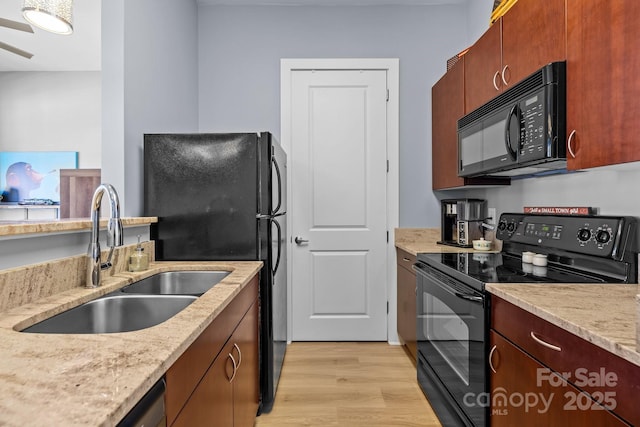 kitchen with a sink, light wood finished floors, black appliances, and light stone countertops