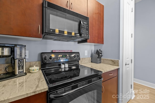 kitchen with baseboards, black appliances, light wood-style flooring, and light stone countertops