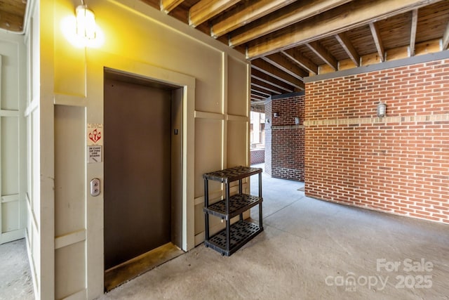 interior space featuring elevator, brick wall, and concrete flooring