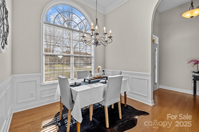 dining room featuring arched walkways, a wainscoted wall, ornamental molding, wood finished floors, and a chandelier