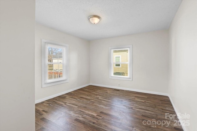 empty room featuring a healthy amount of sunlight, a textured ceiling, and dark hardwood / wood-style floors