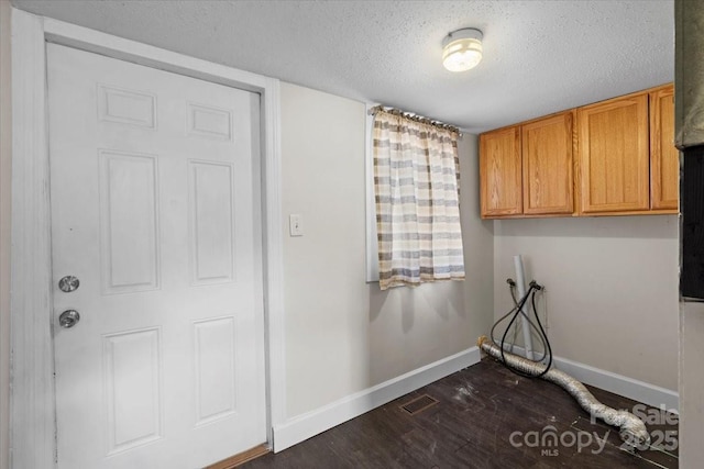 clothes washing area featuring dark wood-type flooring, washer hookup, cabinets, and a textured ceiling