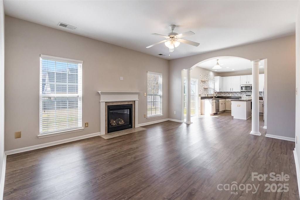 unfurnished living room featuring dark wood-style flooring, decorative columns, a fireplace, visible vents, and ceiling fan