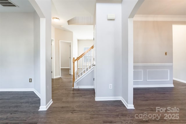 interior space with arched walkways, wood finished floors, visible vents, baseboards, and ornamental molding