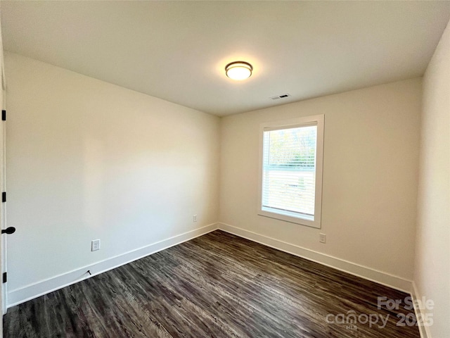 spare room featuring dark wood-style flooring, visible vents, and baseboards