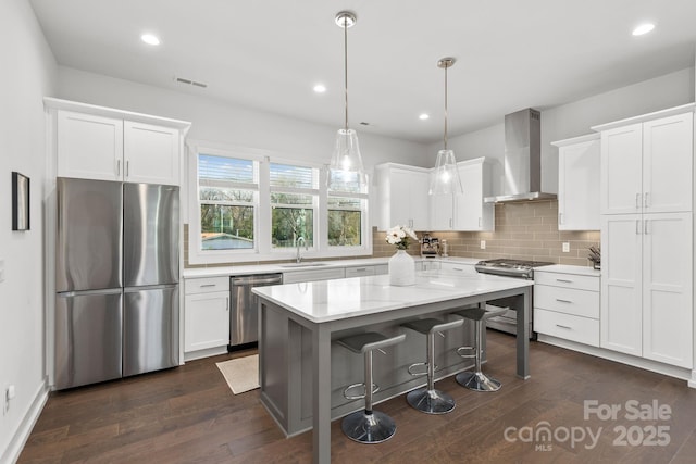 kitchen featuring stainless steel appliances, a sink, white cabinetry, a center island, and wall chimney exhaust hood