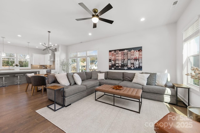 living area featuring ceiling fan with notable chandelier, recessed lighting, visible vents, and wood finished floors