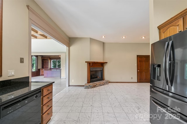 kitchen featuring dark stone countertops, black dishwasher, a stone fireplace, and stainless steel refrigerator with ice dispenser