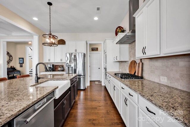 kitchen with wall chimney range hood, white cabinetry, stainless steel appliances, and light stone counters