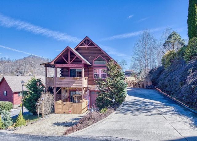 log-style house with stone siding, gravel driveway, fence, and a balcony