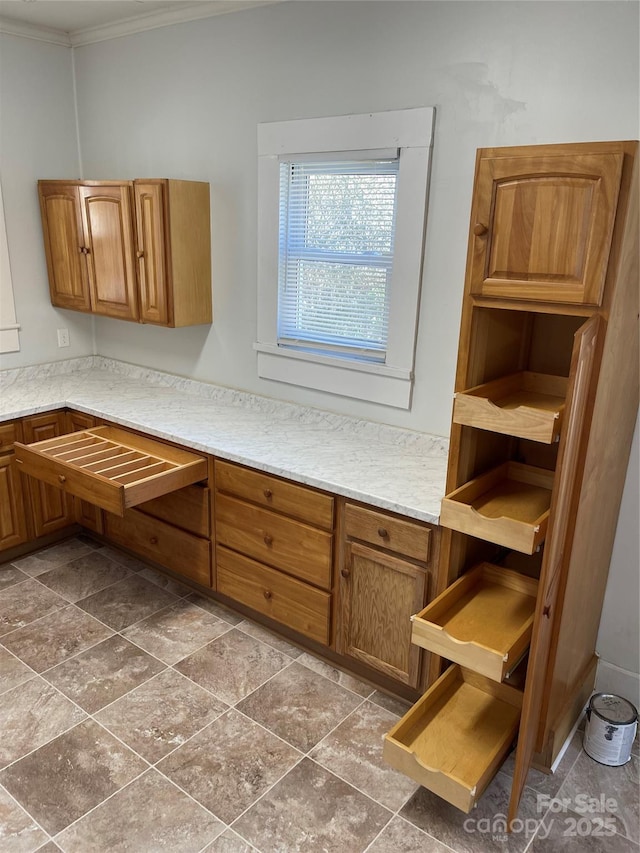 kitchen featuring light stone counters, brown cabinetry, and crown molding