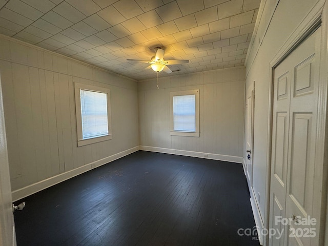 spare room featuring dark wood-type flooring, a wealth of natural light, baseboards, and a ceiling fan