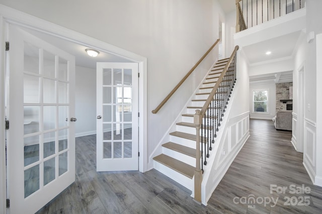 stairs featuring ornamental molding, wood finished floors, a high ceiling, french doors, and a fireplace