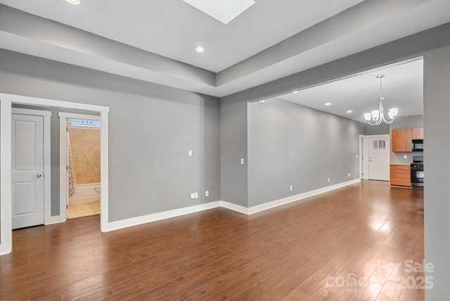 unfurnished living room with dark wood-type flooring, a skylight, and an inviting chandelier