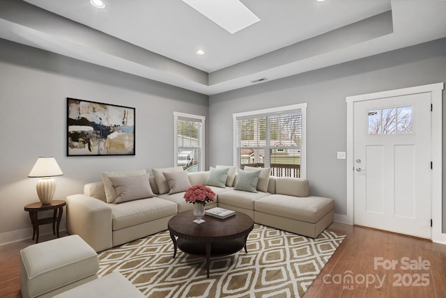 living room with a skylight, hardwood / wood-style floors, and a raised ceiling