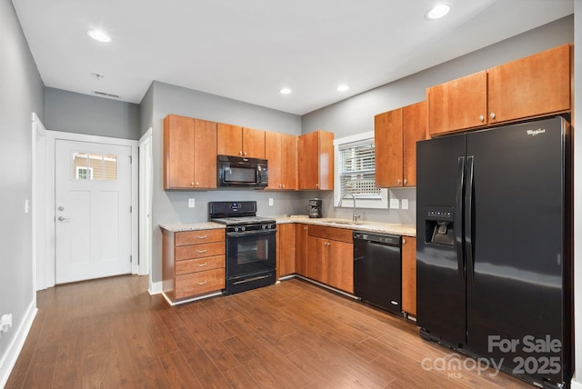 kitchen with sink, light stone counters, wood-type flooring, and black appliances