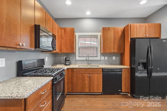 kitchen with light hardwood / wood-style floors, sink, black appliances, and light stone counters