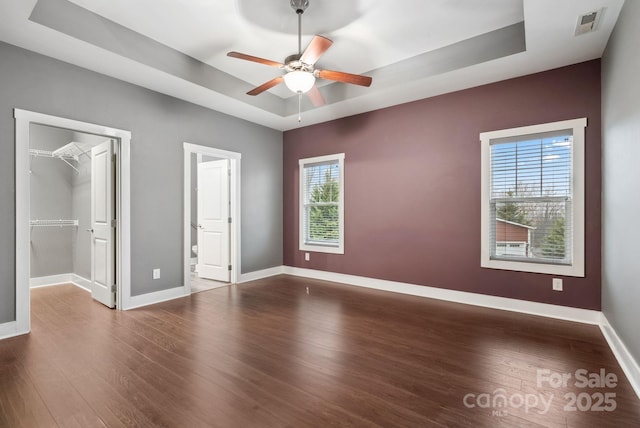 unfurnished bedroom with a closet, a spacious closet, ceiling fan, a raised ceiling, and hardwood / wood-style floors