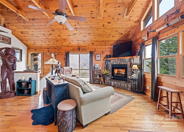 living area with a ceiling fan, wood finished floors, wooden walls, a stone fireplace, and wooden ceiling