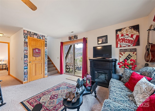 carpeted living area with visible vents, baseboards, a glass covered fireplace, and stairs