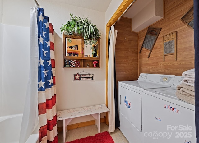 laundry room with light tile patterned floors, laundry area, wood walls, and separate washer and dryer