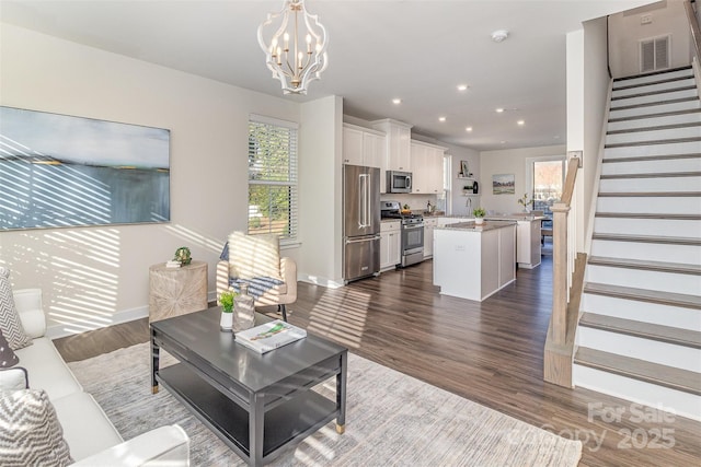 living area featuring stairs, dark wood-style floors, visible vents, and a chandelier