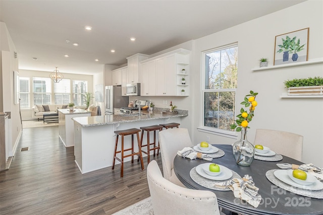 kitchen with a breakfast bar area, appliances with stainless steel finishes, white cabinetry, light stone countertops, and a peninsula