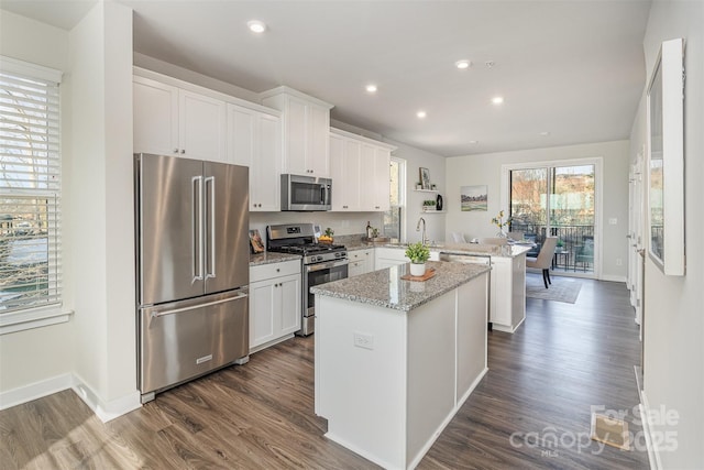 kitchen with a peninsula, appliances with stainless steel finishes, light stone counters, and white cabinets