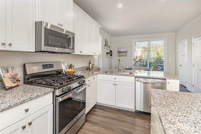 kitchen with light stone counters, dark wood finished floors, stainless steel appliances, white cabinets, and a sink