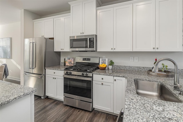 kitchen featuring white cabinets, light stone counters, appliances with stainless steel finishes, dark wood-type flooring, and a sink