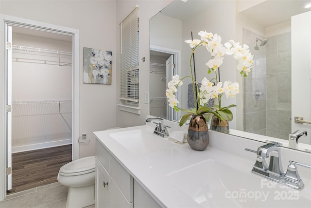 bathroom with toilet, double vanity, a tile shower, and a sink