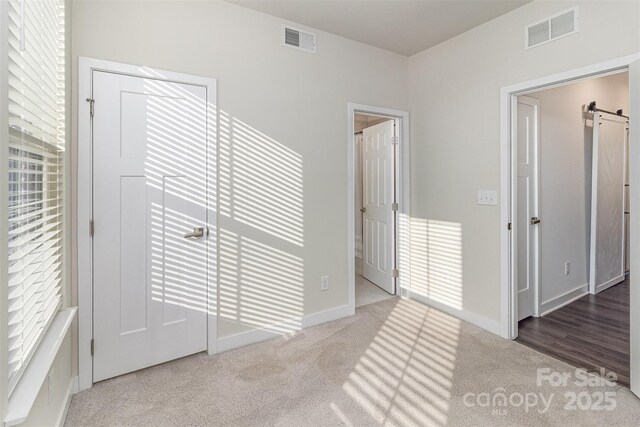 unfurnished bedroom with carpet floors, a barn door, visible vents, and baseboards