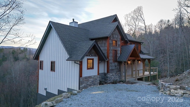 exterior space featuring a shingled roof, a chimney, and a forest view