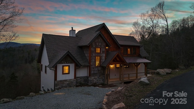 view of front of house featuring covered porch, stone siding, and a chimney