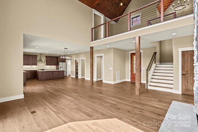 unfurnished living room featuring high vaulted ceiling, wood finished floors, visible vents, baseboards, and stairway