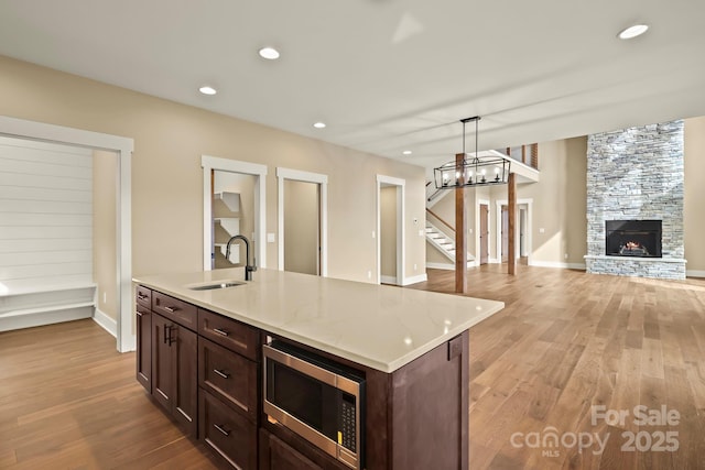 kitchen with a kitchen island with sink, a sink, open floor plan, hanging light fixtures, and stainless steel microwave