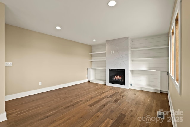 unfurnished living room featuring dark wood-type flooring, recessed lighting, a fireplace, and baseboards