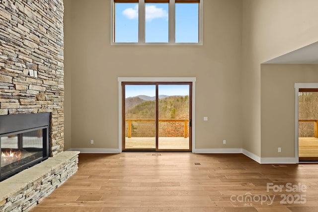 unfurnished living room with a mountain view, a high ceiling, a fireplace, baseboards, and light wood finished floors