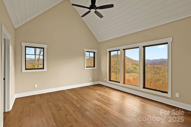 unfurnished room featuring baseboards, ceiling fan, wood finished floors, high vaulted ceiling, and a mountain view