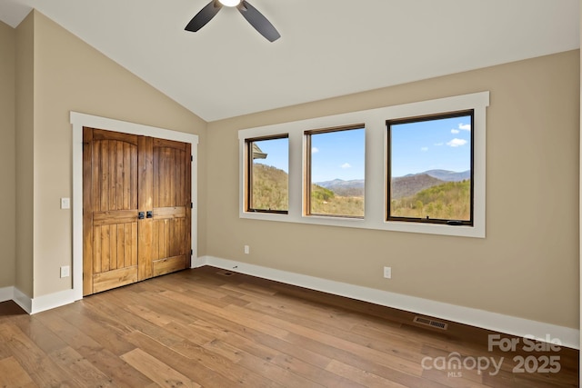 unfurnished bedroom featuring visible vents, baseboards, vaulted ceiling, light wood-style floors, and a mountain view