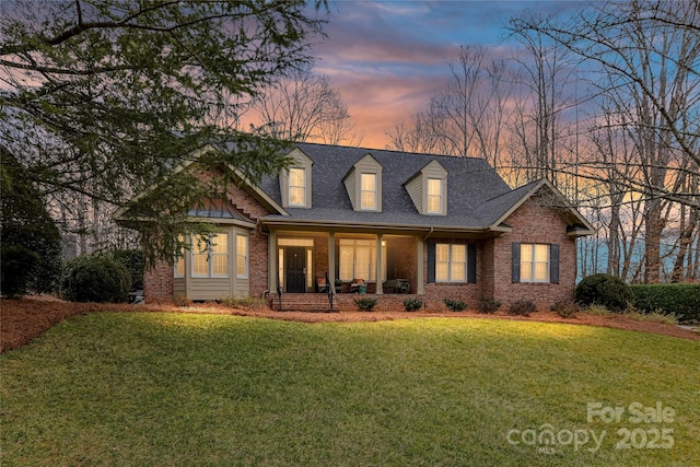 new england style home with roof with shingles, a lawn, and brick siding