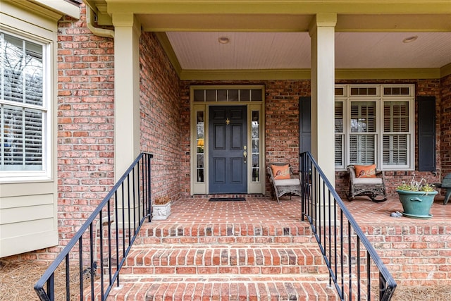 doorway to property featuring a porch and brick siding