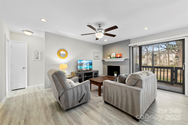 living room with light wood-type flooring, ceiling fan, and a fireplace