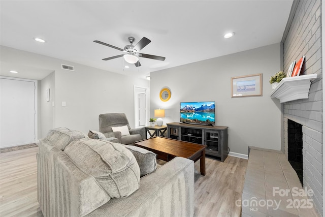 living room with a brick fireplace, light hardwood / wood-style floors, and ceiling fan