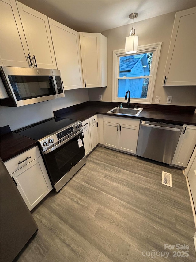 kitchen featuring white cabinetry, hanging light fixtures, appliances with stainless steel finishes, and sink