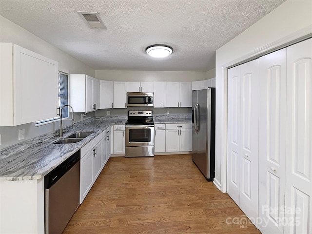 kitchen featuring stainless steel appliances, visible vents, white cabinets, a sink, and wood finished floors