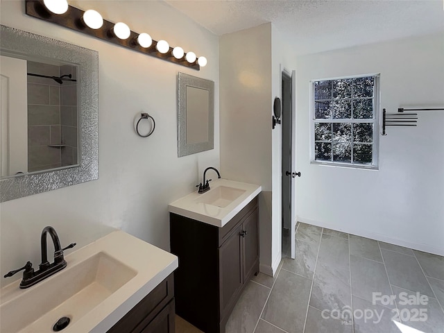 full bathroom featuring a textured ceiling, baseboards, two vanities, and a sink